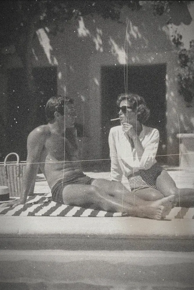Un couple assis sur une serviette rayée au bord d'une piscine